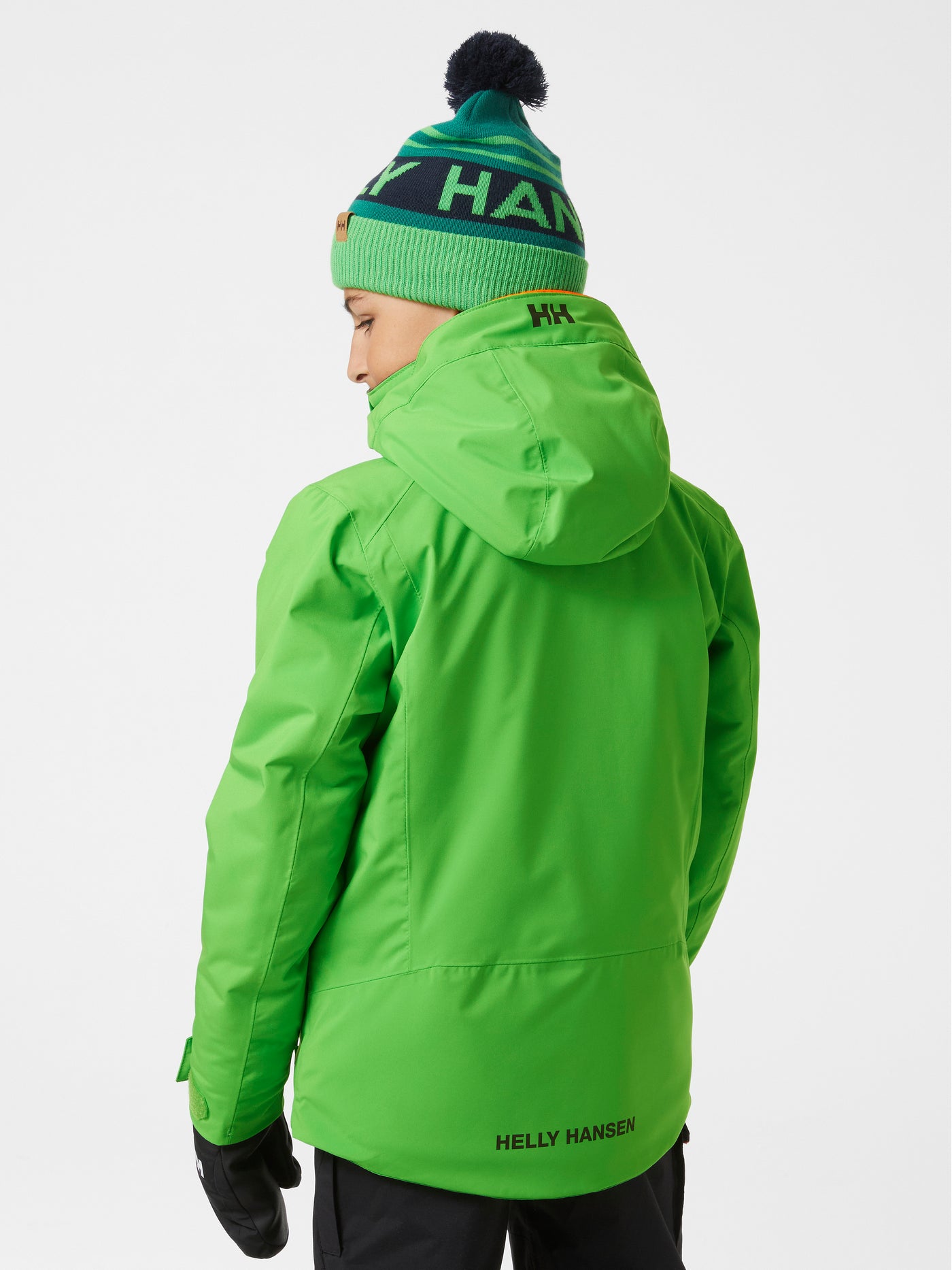 Helly Hansenin lasten ja nuorten Alpha-laskettelutakki kirkkaan vihreässä sävyssä lapsen päällä takaa kuvattuna