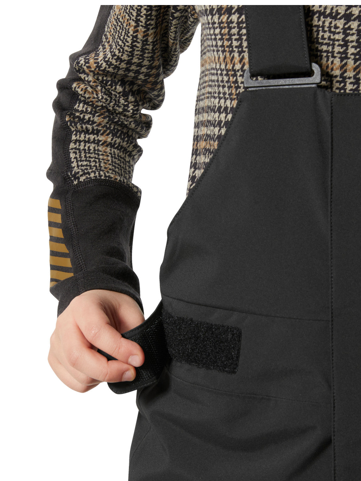 Helly Hansenin mustat lasten ja nuorten korkeavyötäröiset Bib pants -lasketteluhousut lapsen päällä, lähikuvassa vyötärön kiristysmekanismi.