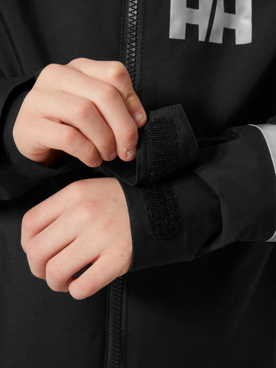 Helly Hansenin musta Jr Shelter HT Jacket, lasten  ja nuorten välikausitakki, kuva hihansuusta lapsen päällä