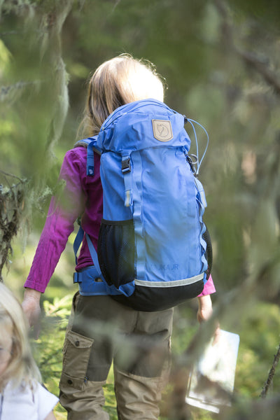 Tytön selässä metsässä Fjällrävenin Kajka Jr lasten rinkka värissä UN Blue takaa kuvattuna