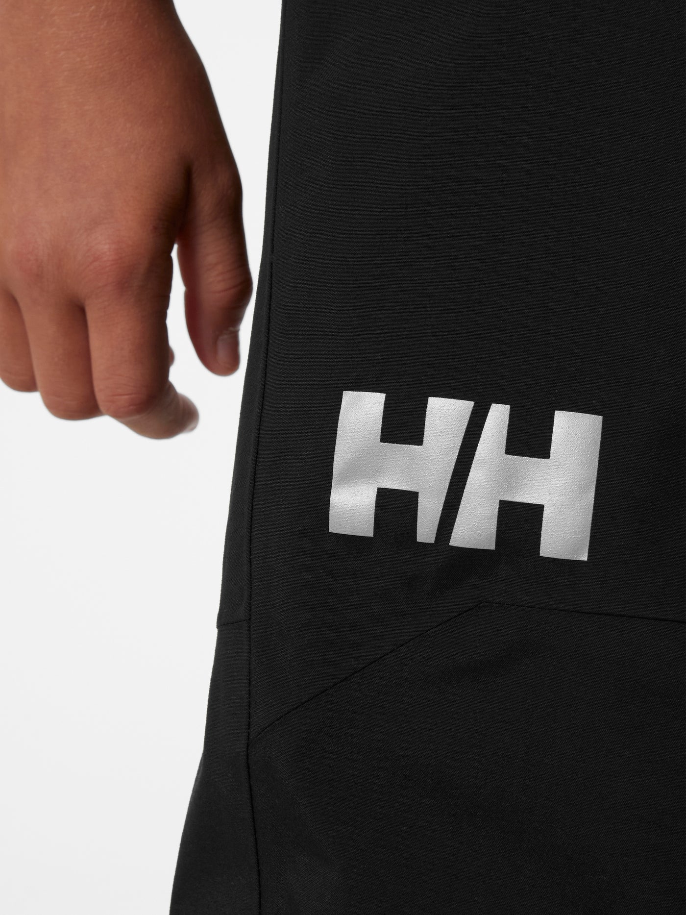 Helly Hansen Junior Guard Pant nuorten mustat kuorihousut lähikuva HH-logosta
