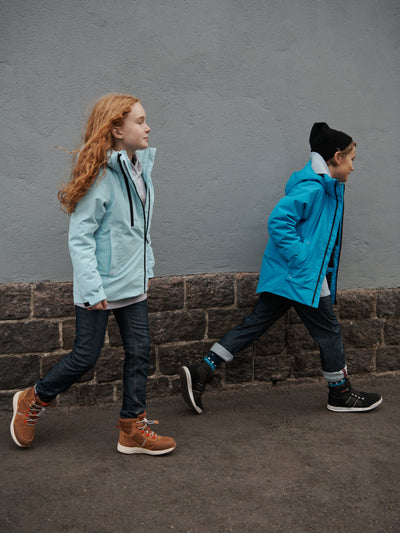 Reiman Reimatec Perille -laskettelutakki turkoosin sävyssä lapsen päällä kaupungissa, joka kävelee toisen lapsen kanssa