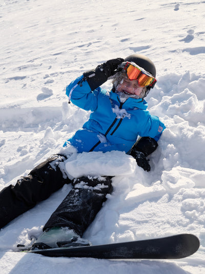 Sininen Reiman Reimatec Tieten -laskettelutakki lumessa makaavalla lapsella päällä